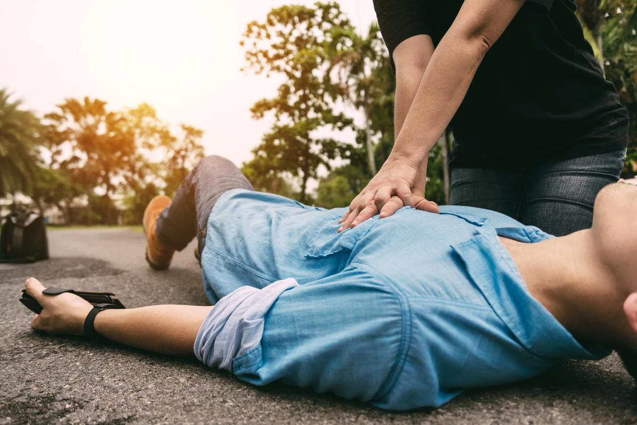 A person performs chest compressions on an unconscious man outdoors. (Adobe Stock Photo)