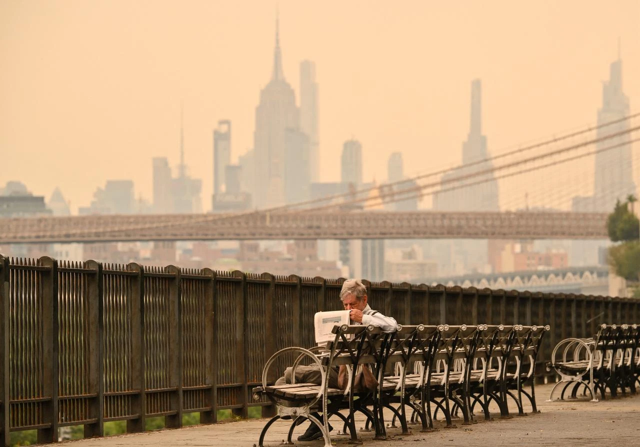 A man reads a newspaper along the Brooklyn waterfront as Canadian wildfire smoke shrouds the Manhattan skyline in New York City, U.S., July 16, 2026. (AFP Photo)