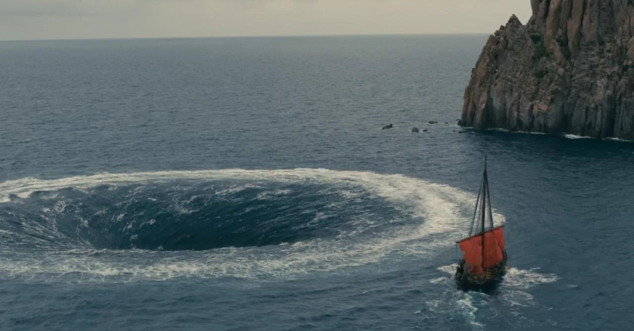 A scene from "The Odyssey" shows an ancient sailing vessel approaching a whirlpool near a rocky coastline. (Photo via IMDb)