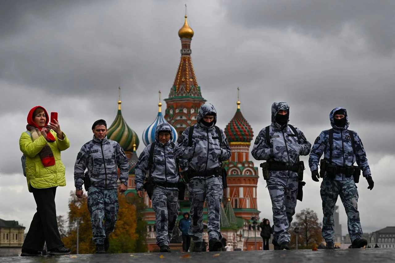 A woman uses her smartphone as riot policemen walk along Red Square in front of St. Basil's Cathedral on an autumn day in central Moscow on October 14, 2025. (AFP Photo)