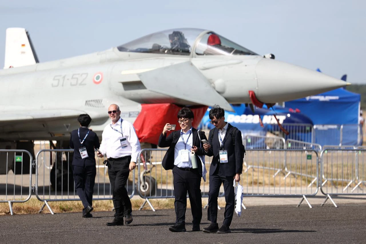 Delegates stand in front of an Italian Air Force Eurofighter Typhoon as they arrive to attend the opening day of the Farnborough International Airshow 2026 in in Farnborough, south-west of London, July 20, 2026. (AFP Photo)