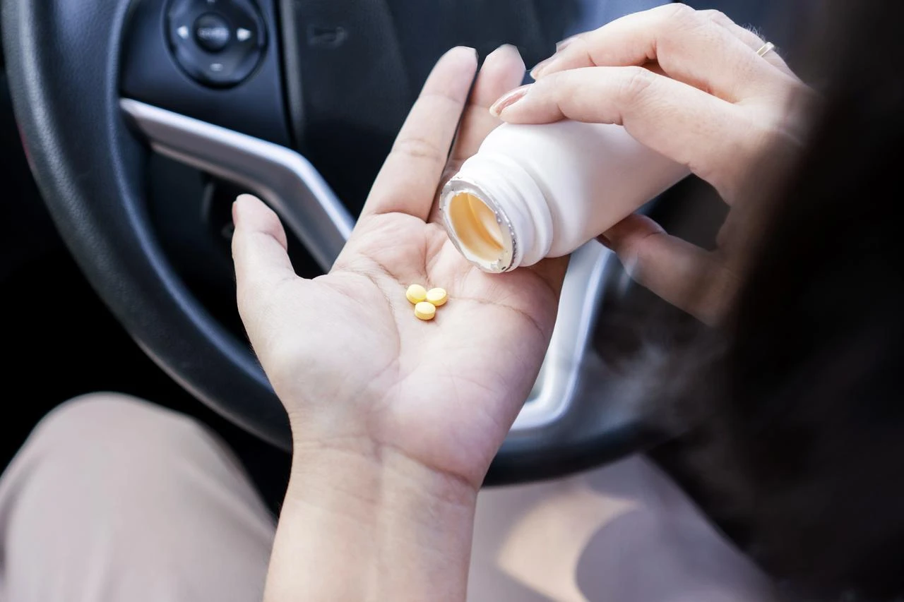 A person pours pills from an unlabeled bottle into their hand while seated in a car. (Adobe Stock Photo)