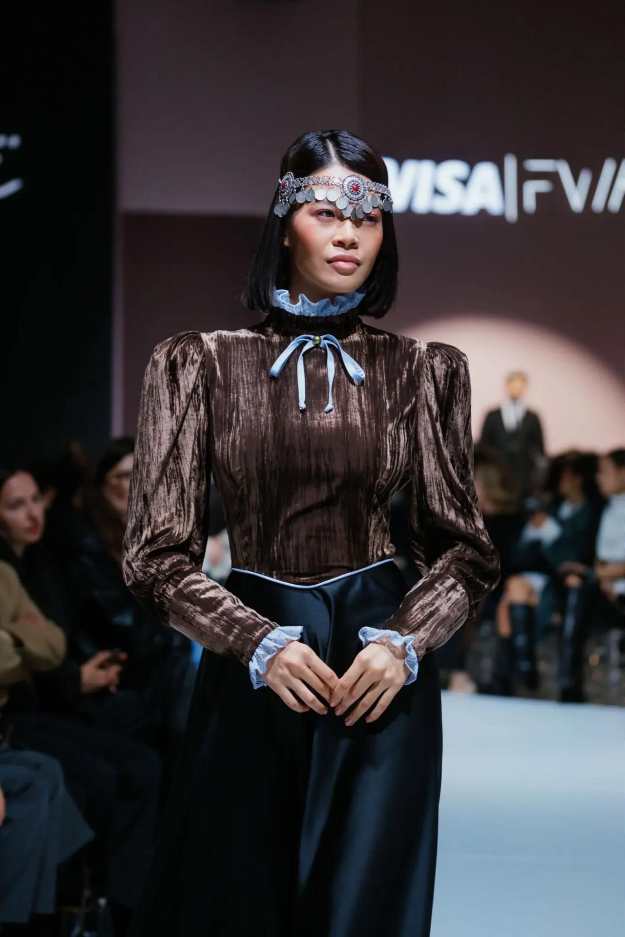 A model showcases a high-neck textured velvet blouse and a traditional coin headpiece on the runway at VISA Fashion Week at Visa Fashion Week Almaty in Kazakhstan.
