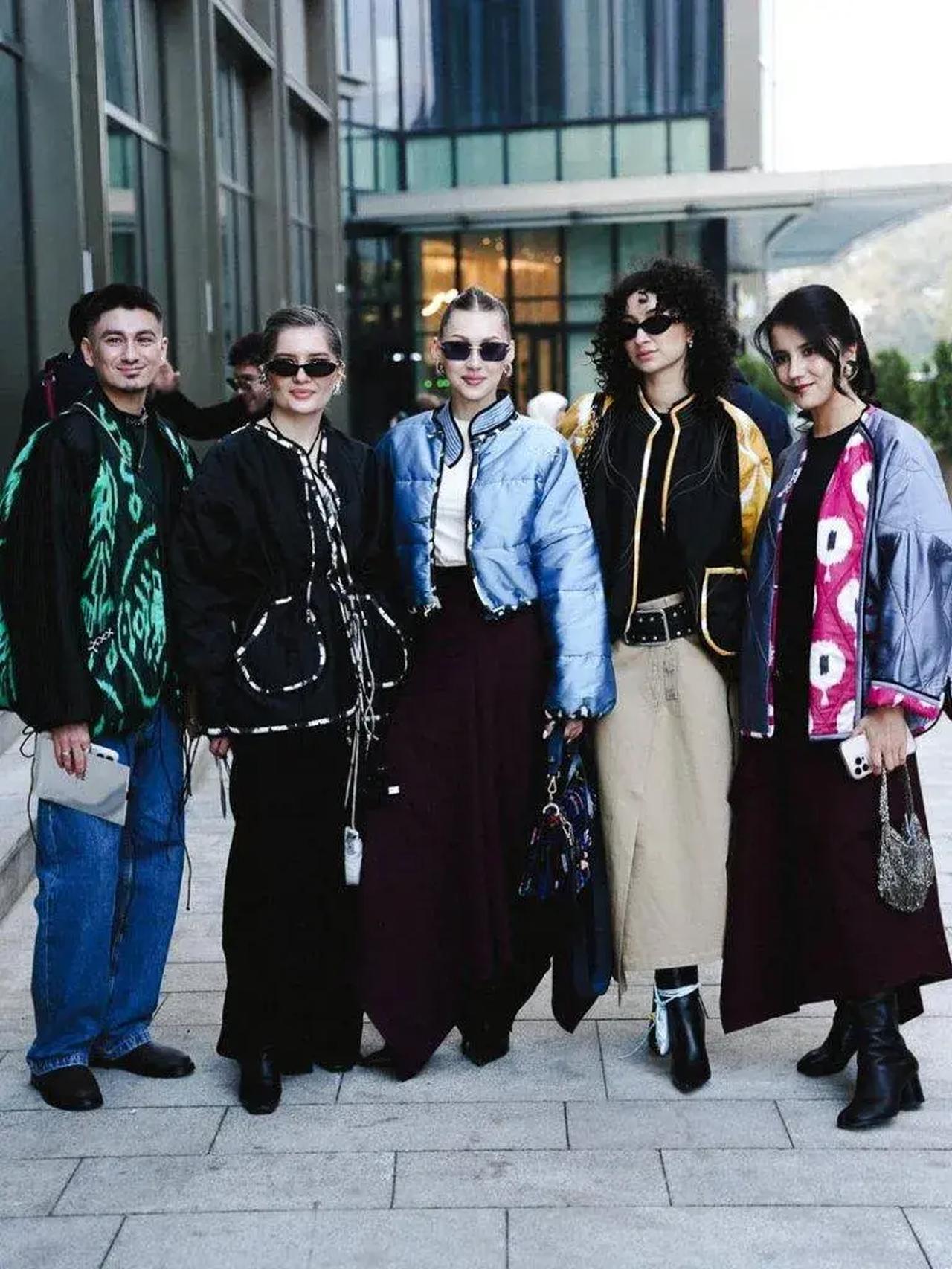 Street style outside a fashion event—five attendees in a mix of embroidered jackets, wide-leg trousers, and statement sunglasses, the kind of "impromptu" look built for the cameras waiting outside. Almaty, Kazakhstan.