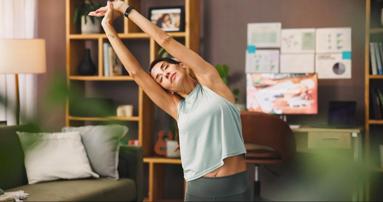 A woman stretches her upper body while exercising at home. (Adobe Stock Photo)