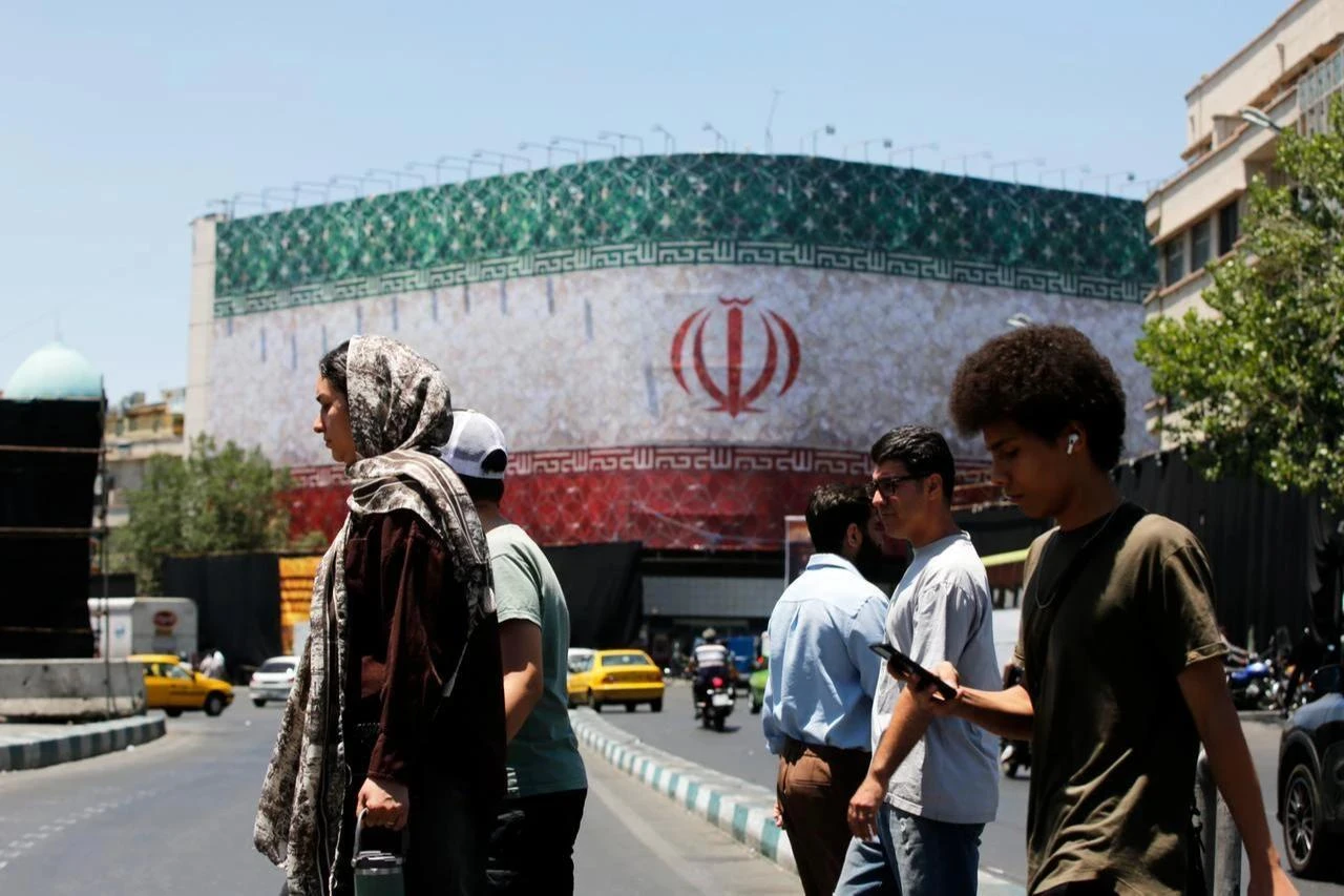 People walk past a billboard displaying Iran's national flag at Enghelab Square in Tehran, Iran, on June 15, 2026. (AA Photo)