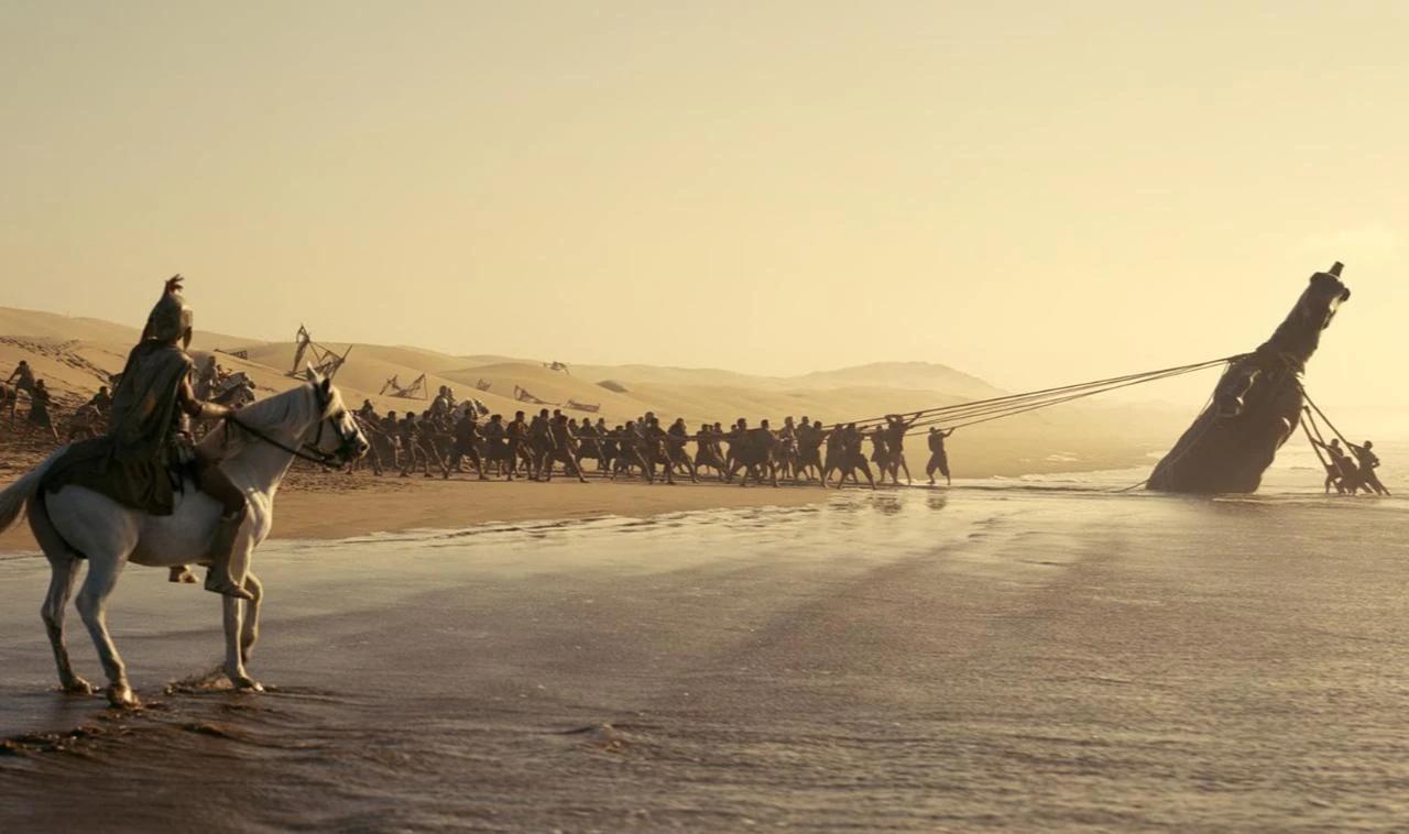 A scene from Christopher Nolan's "The Odyssey" shows a Trojan Horse-like structure being pulled along a shoreline. (Photo via IMDb)