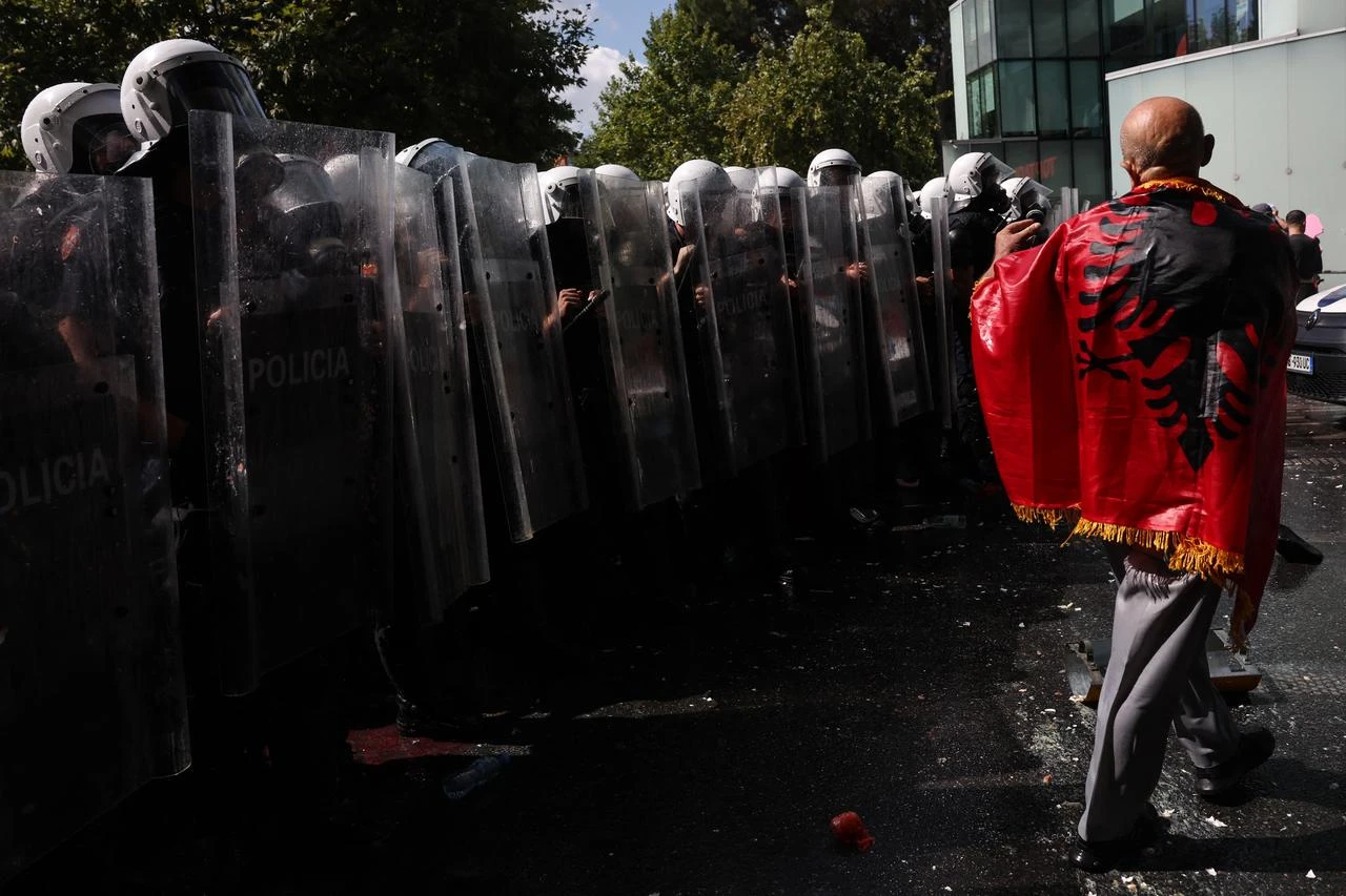 A protester wrapped in the Albanian flag faces police officers during a demonstration outside the parliament in Tirana, on July 23, 2026 as part of a wave of protest against recent government decisions. (AFP Photo)
