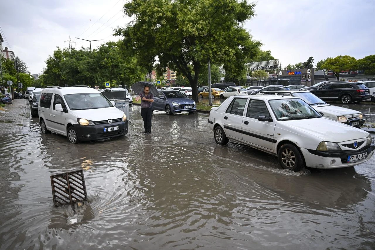 Vehicles move through a flooded street as a pedestrian walks with an umbrella following heavy rainfall during summer in Ankara, Türkiye, on July 25, 2026. (AA Photo)