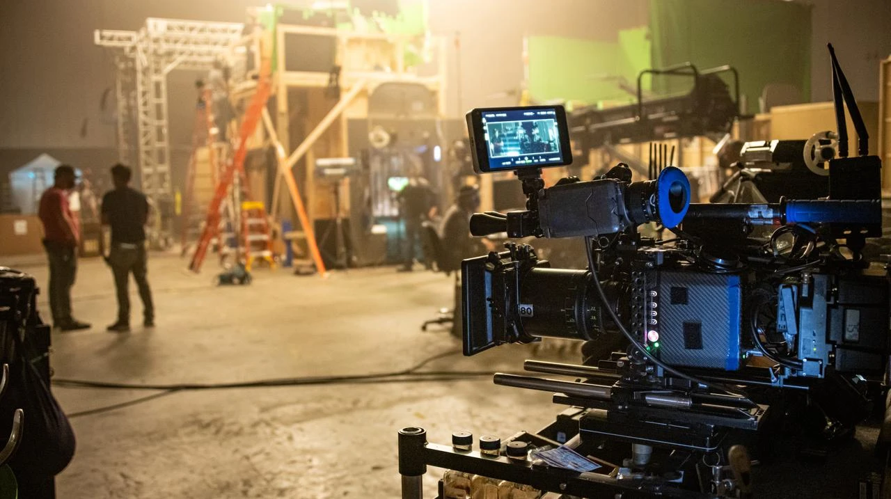 A professional cinema camera is positioned on a busy film production set as crew members prepare equipment in the background. (Adobe Stock Photo)