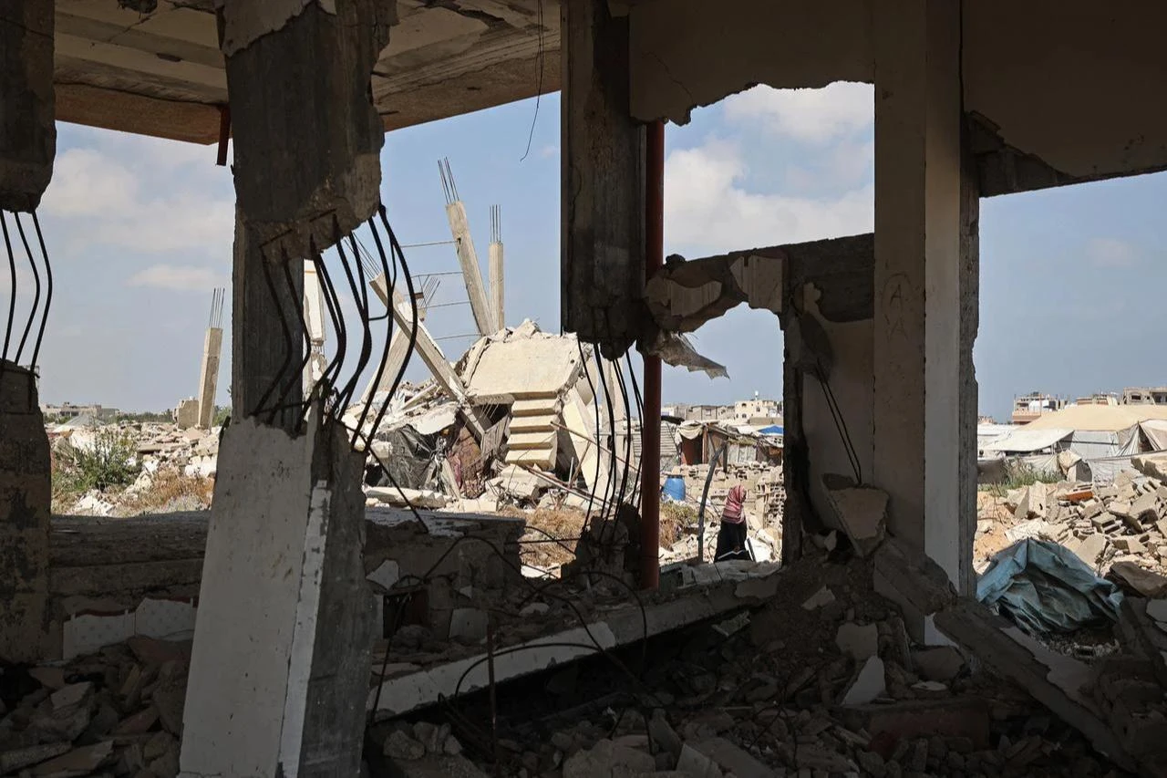 A displaced Palestinian woman walks past destroyed buildings in the east of Deir al-Balah, central Gaza Strip on July 22, 2026, as violence has continued in Gaza despite the ceasefire. (AFP Photo)