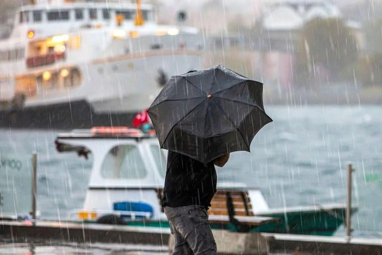 A person walks with an umbrella during heavy rain in Istanbul as boats move along the waterfront. (Photo via the Istanbul Metropolitan Municipality)