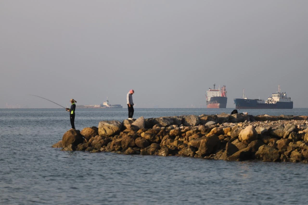 In this picture obtained from Iran's ISNA news agency, residents fish from the shore as cargo and commercial vessels lie at anchor in the Strait of Hormuz off Bandar Abbas, June 8, 2026. (AFP Photo)