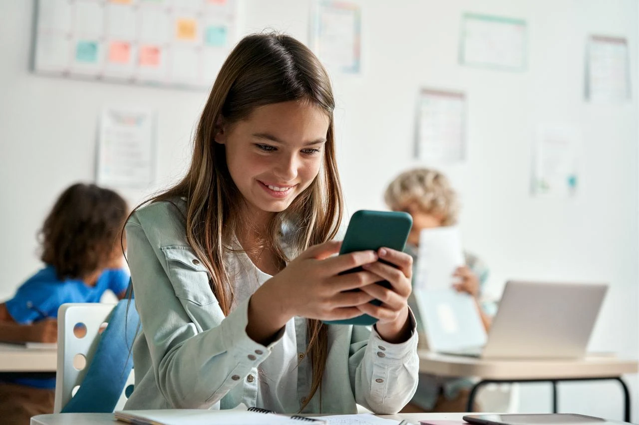 A child looks at a smartphone in a classroom. (Adobe Stock Photo)
