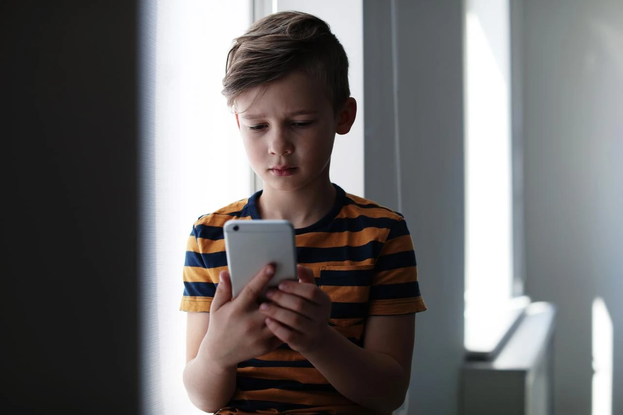 A child looks at a smartphone indoors. (Adobe Stock Photo)