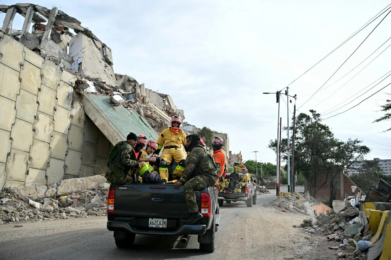 Brazilian rescuers ride in the back of pickup trucks past collapsed buildings as they head to carry out search and rescue operations in La Guaira, Venezuela, July 4, 2026. (AFP Photo)