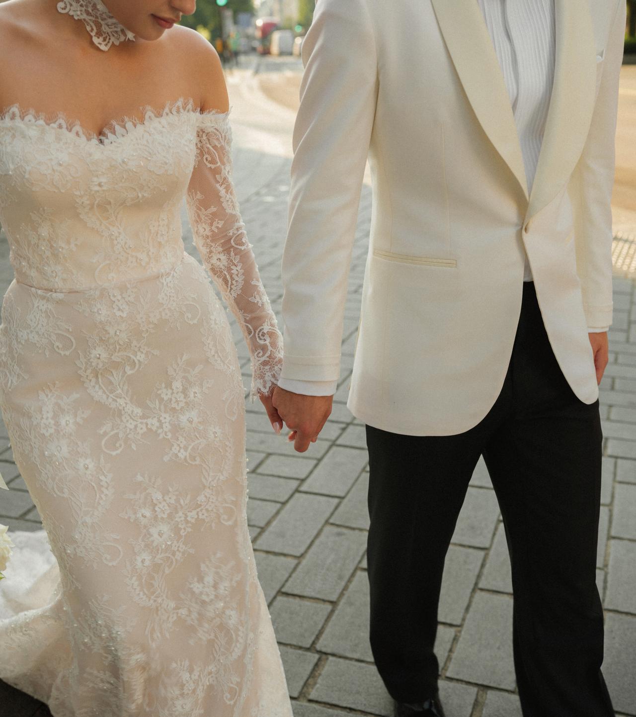 A close-up from Asena Atalar and Ahmed Kutucu's wedding shoot shows the couple holding hands, highlighting Atalar's lace bridal gown and Kutucu's white tuxedo jacket. (Photo via Instagram/@asenatalar and @ahmedkutucu)
