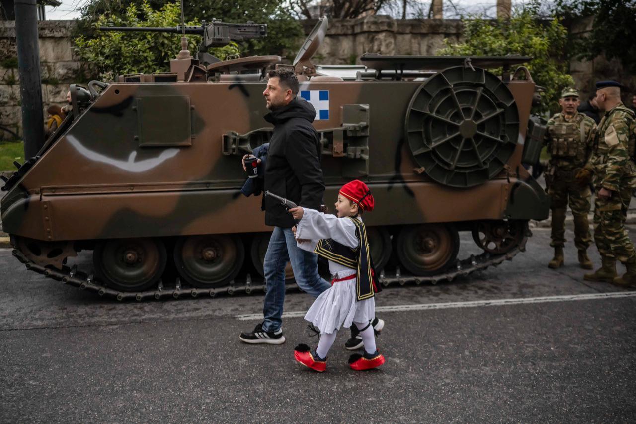 A man with his child dressed in a Greek traditional uniform walks in front of an armored vehicle before a military parade in Athens, March 25, 2026. (AFP Photo)