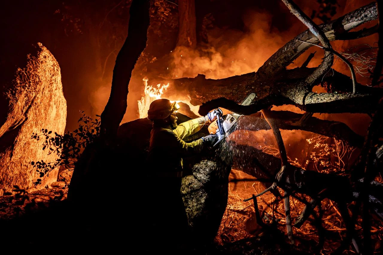 A firefighter uses a chainsaw to cut through burning trees during overnight wildfire suppression operations in La Adrada, in Spain's Avila province, on July 26, 2026. (AA Photo)