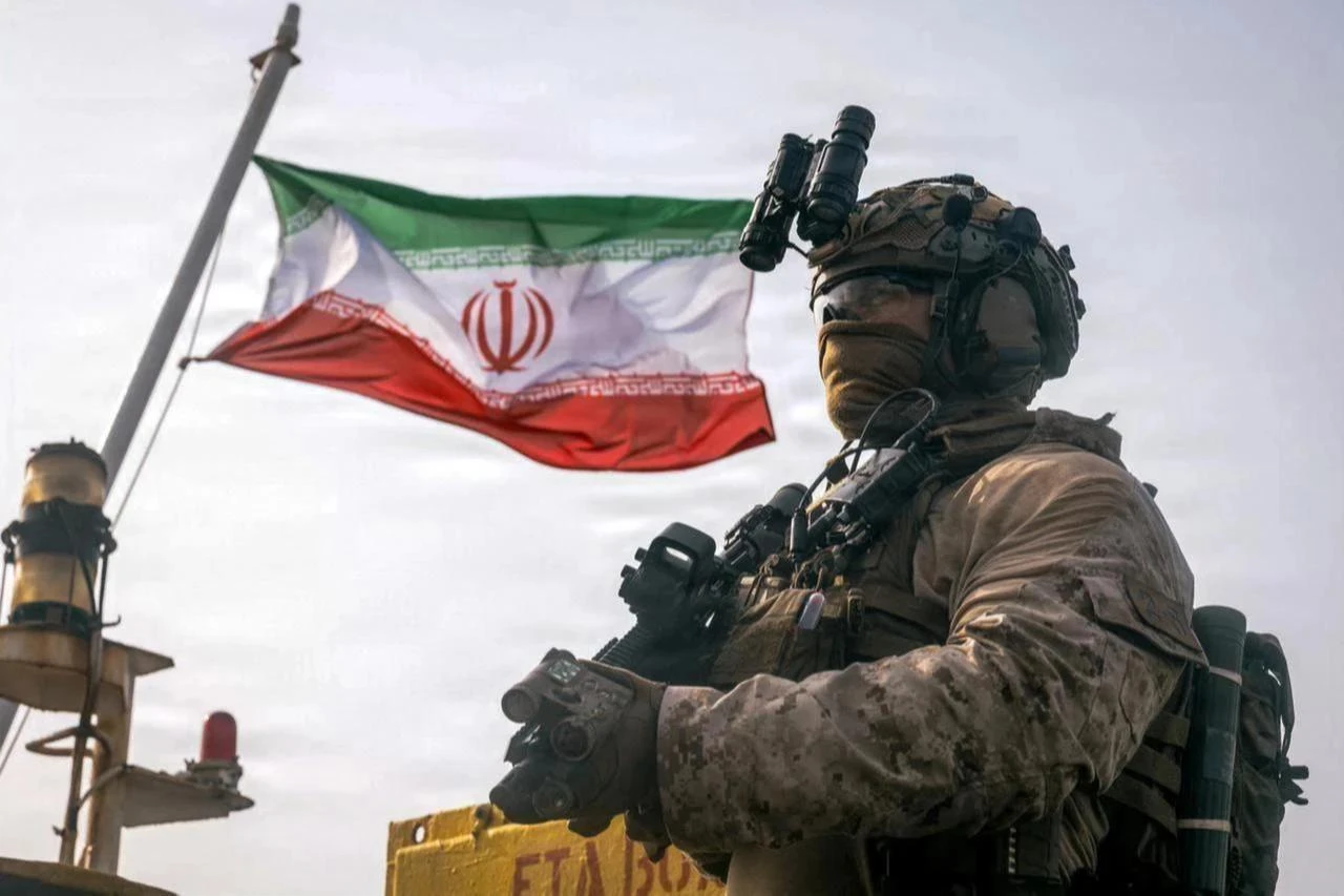 This US Marine Corps handout photograph taken on July 16, 2026, by US Central Command Public Affairs reportedly shows an Iranian flag flying behind a US Marine from the 11th Marine Expeditionary Unit during a verification boarding aboard M/T Wen Yao in the Gulf of Oman. (Photo by Sgt. Joseph Helms / US MARINE CORPS / AFP)