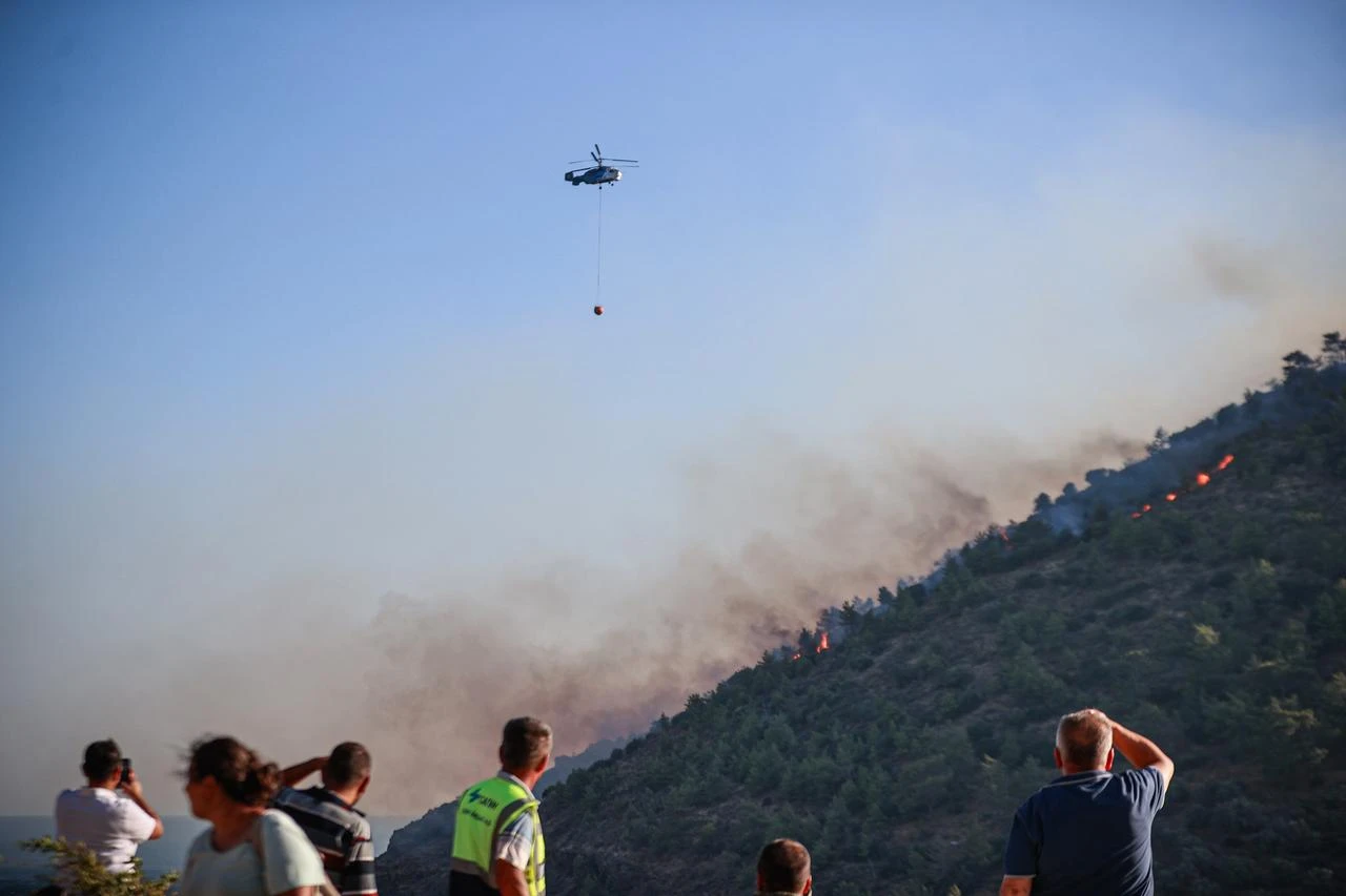 A helicopter drops water on the affected area to extinguish remaining hotspots as firefighting crews carry out cooling operations after largely containing a forest fire through aerial and ground interventions in the Aydincik district of Mersin, Türkiye, on July 30, 2026. (AA Photo)
