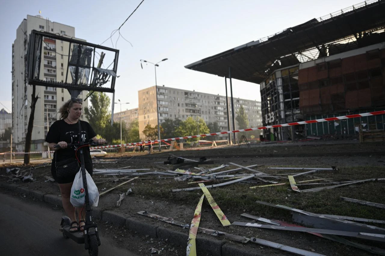 A woman rides an electric scooter past a damaged supermarket following a missile strike in the Ukrainian capital of Kyiv on August 1, 2026. (AFP Photo)