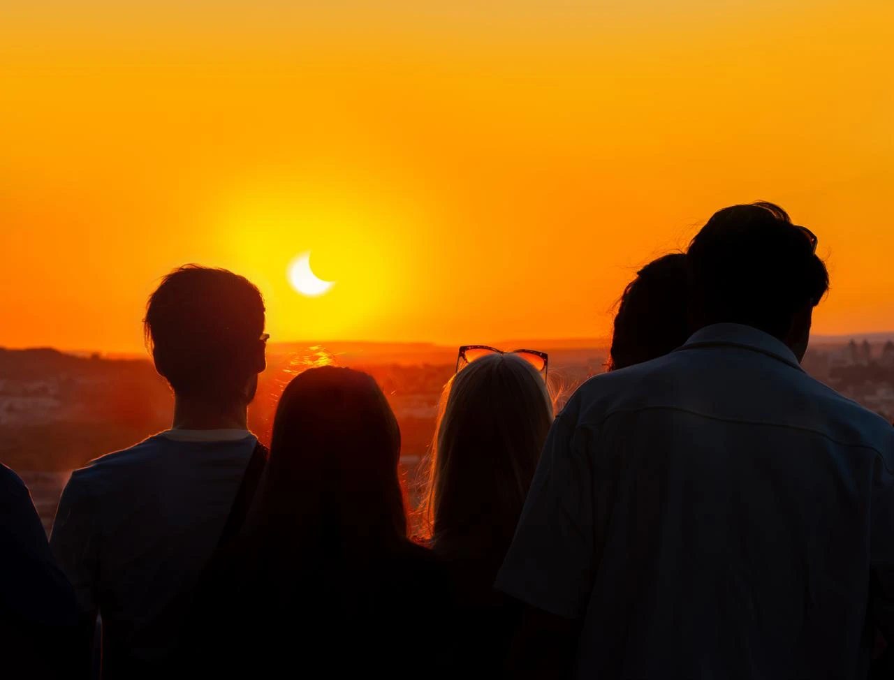 Silhouettes of people backlit by the light, observing a partial solar eclipse at sunset from the top of the Eiffel Tower. (Photo via Adobe Stock)