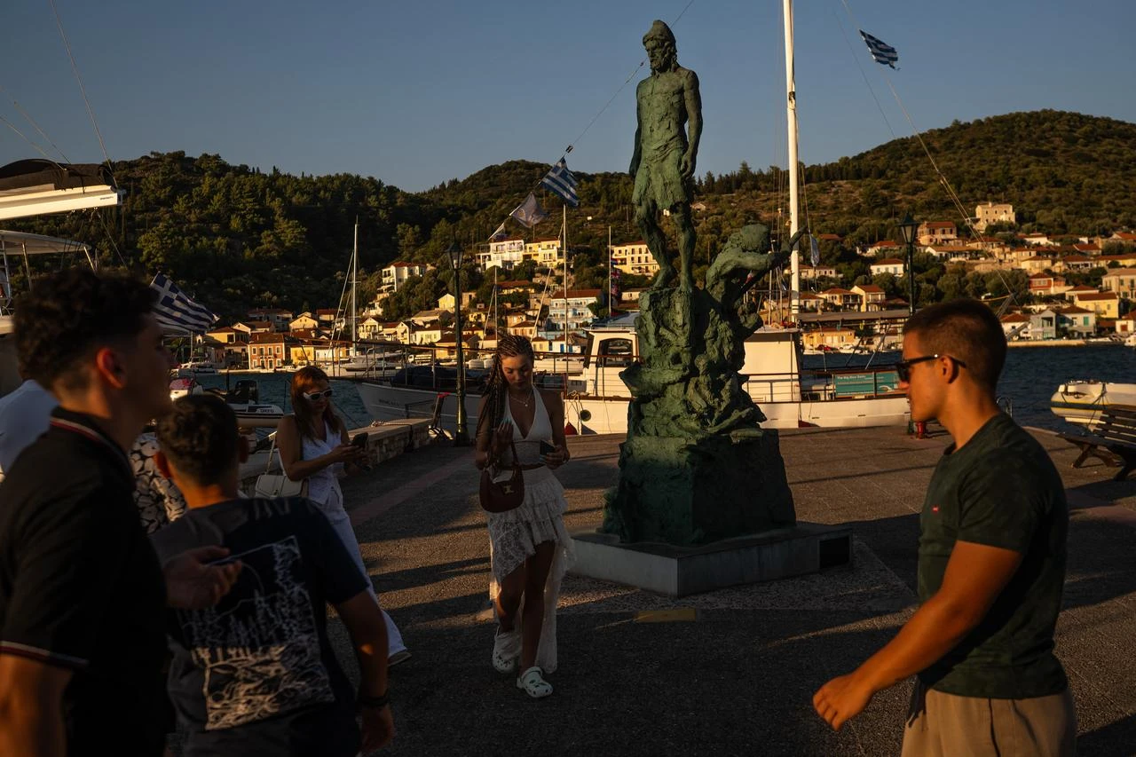 Tourists stand next to a statue of Odysseus, sculpted by Korina Cassianou, in the town of Vathy on the island of Ithaca, in the Ionian Sea, on August 3, 2026. (AFP Photo)