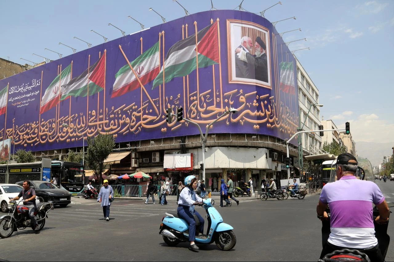 People walk past a giant banner as daily life continues amid ongoing tensions between the United States and Iran on August 6, 2026. (AA Photo)