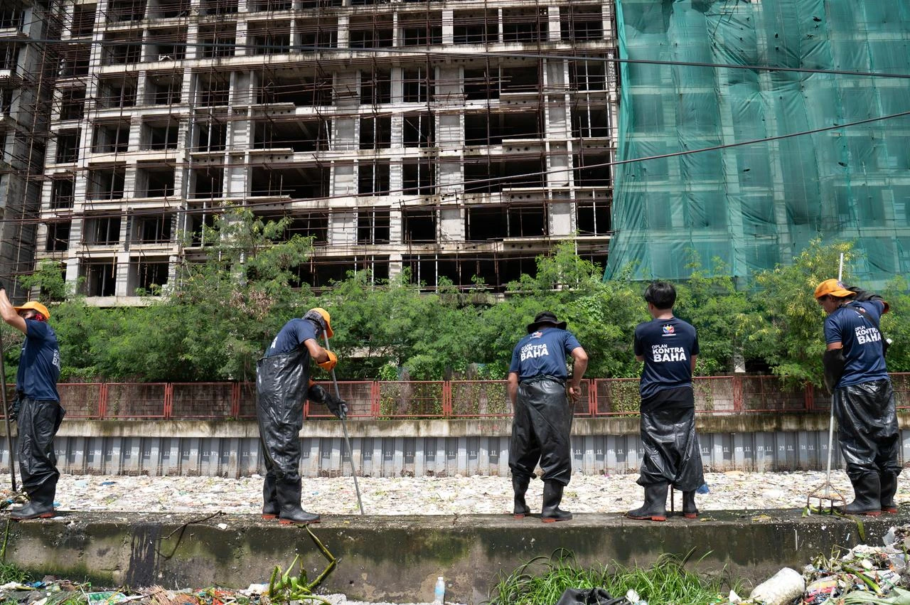 Workers scoop rubbish washed up on a river at the height of heavy rains enhanced by the Southwest monsoon days before, near a shopping complex in Paranaque City, suburban Manila on August 11, 2026. (AFP Photo)