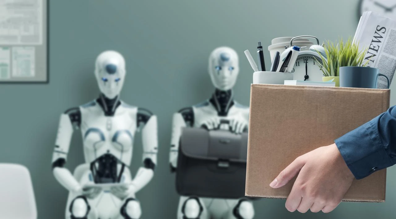 Fired office worker holding a box with belongings and leaving the office, humanoid AI robots waiting for a job interview in the background. (Photo via Adobe Stock)