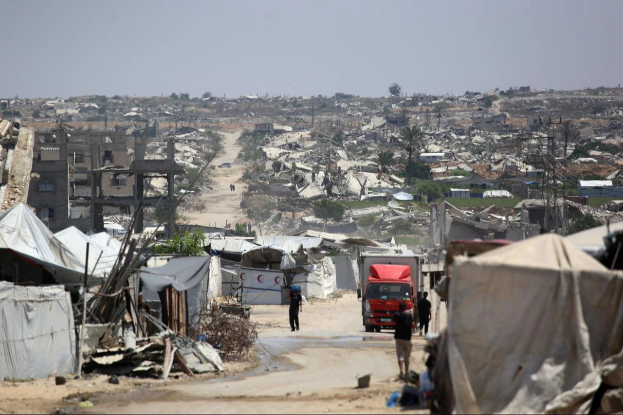 Internally displaced Palestinians walk past tents housing them and the rubble of buildings destroyed by the Israeli military in the distance, in Khan Yunis, southern Gaza Strip, August 11, 2026. (AFP Photo)