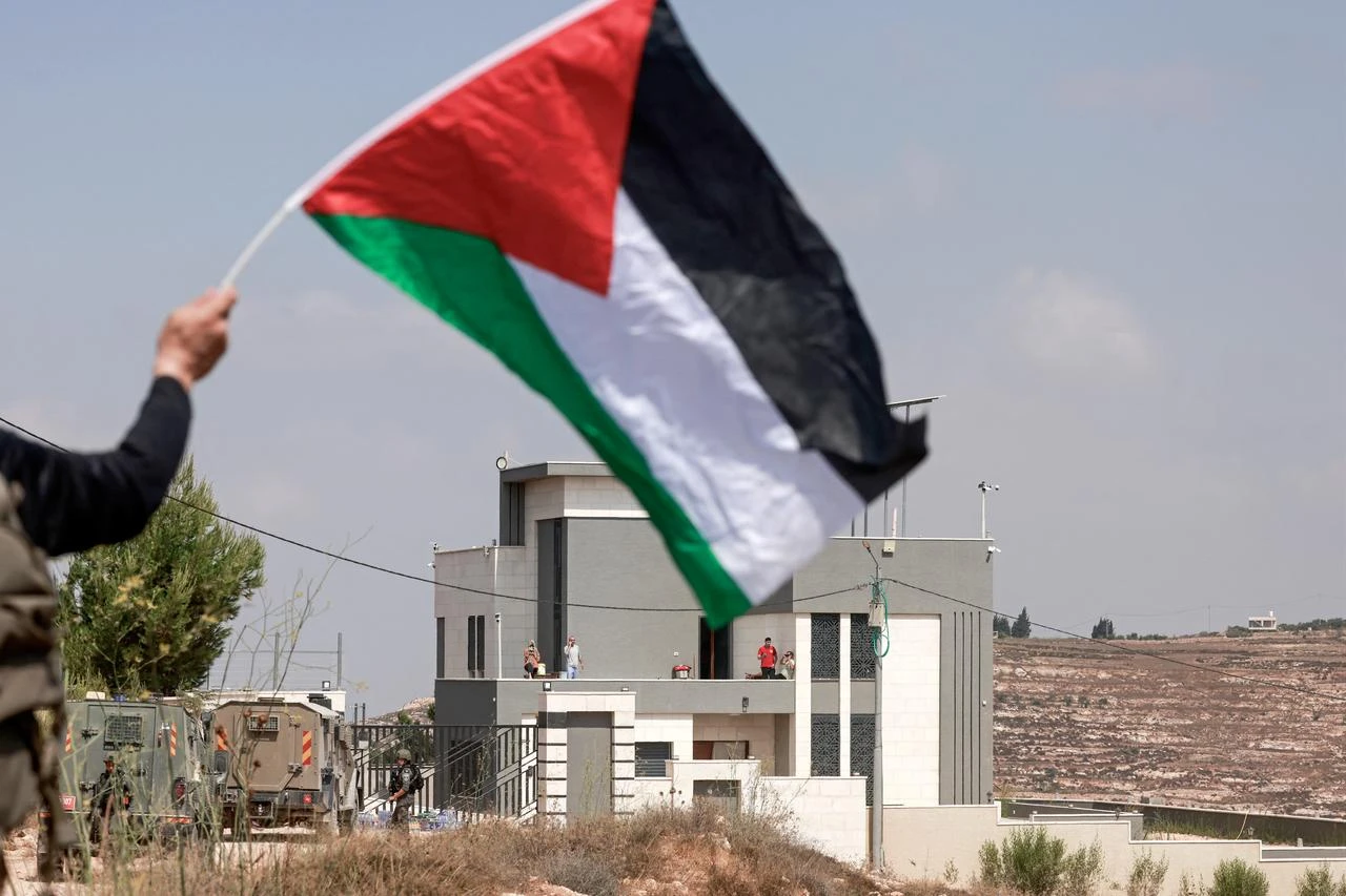A man waves Palestinian flag in front of a Palestinian house besieged by Israeli illegal settlers in the village of Qusra, south of Nablus, in the occupied West Bank, on August 14, 2026. (AFP Photo)