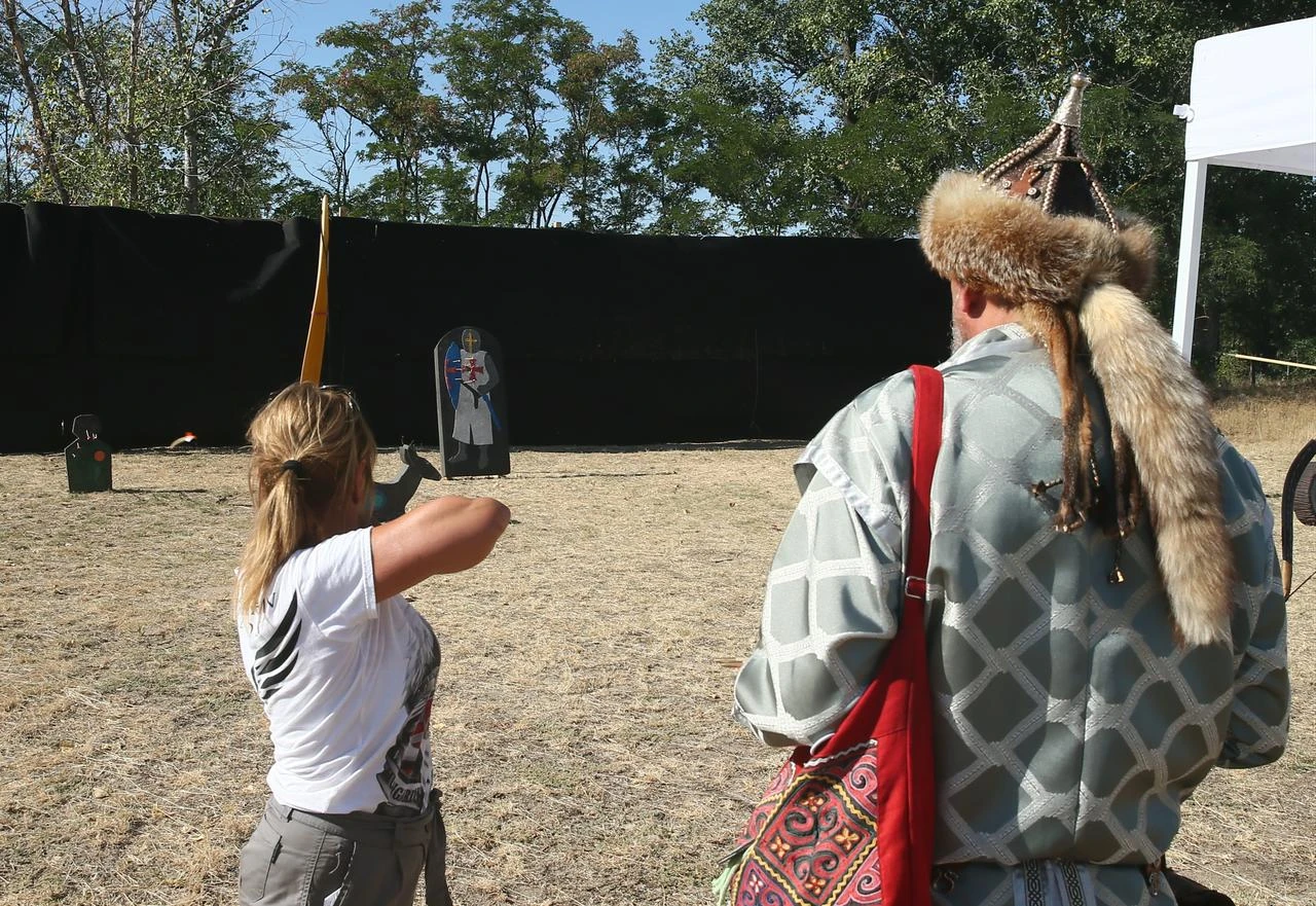 A visitor tries traditional archery alongside a participant in traditional attire during the Great Hun-Turkic Kurultaj in Bugac, Hungary. (AA Photo)