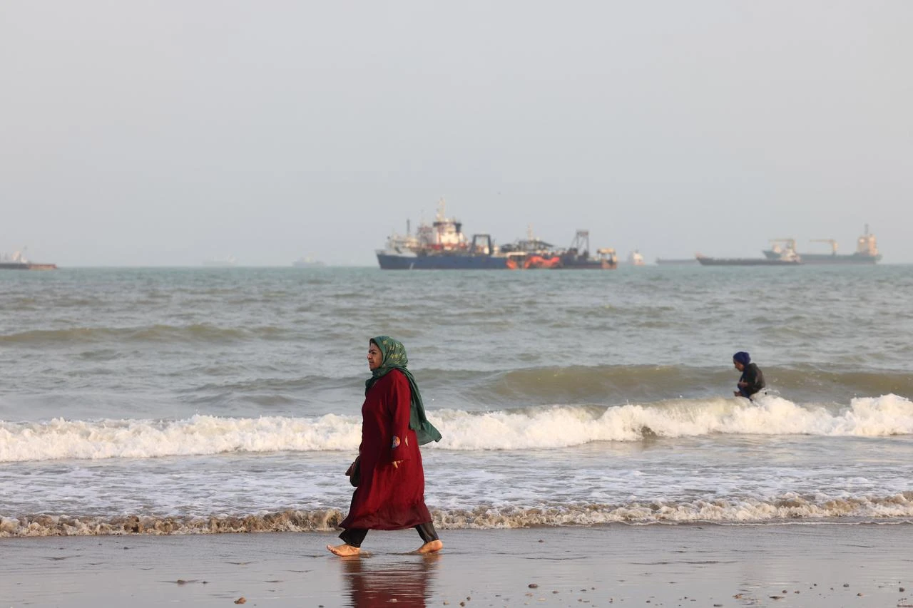 An Iranian woman walks along the seashore as vessels are seen in the Strait of Hormuz off Bandar Abbas, in southern Iran on August 10, 2026. (AFP Photo)