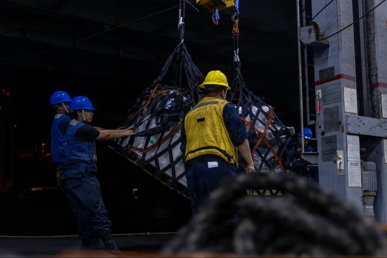 U.S. Sailors receive cargo during a replenishment-at-sea with Lewis and Clark-class dry cargo and ammunition ship USNS Cesar Chavez (T-AKE-14) in the hangar bay of Nimitz-class aircraft carrier USS Abraham Lincoln (CVN 72), Aug. 1, 2026. (Photo via U.S. Navy)