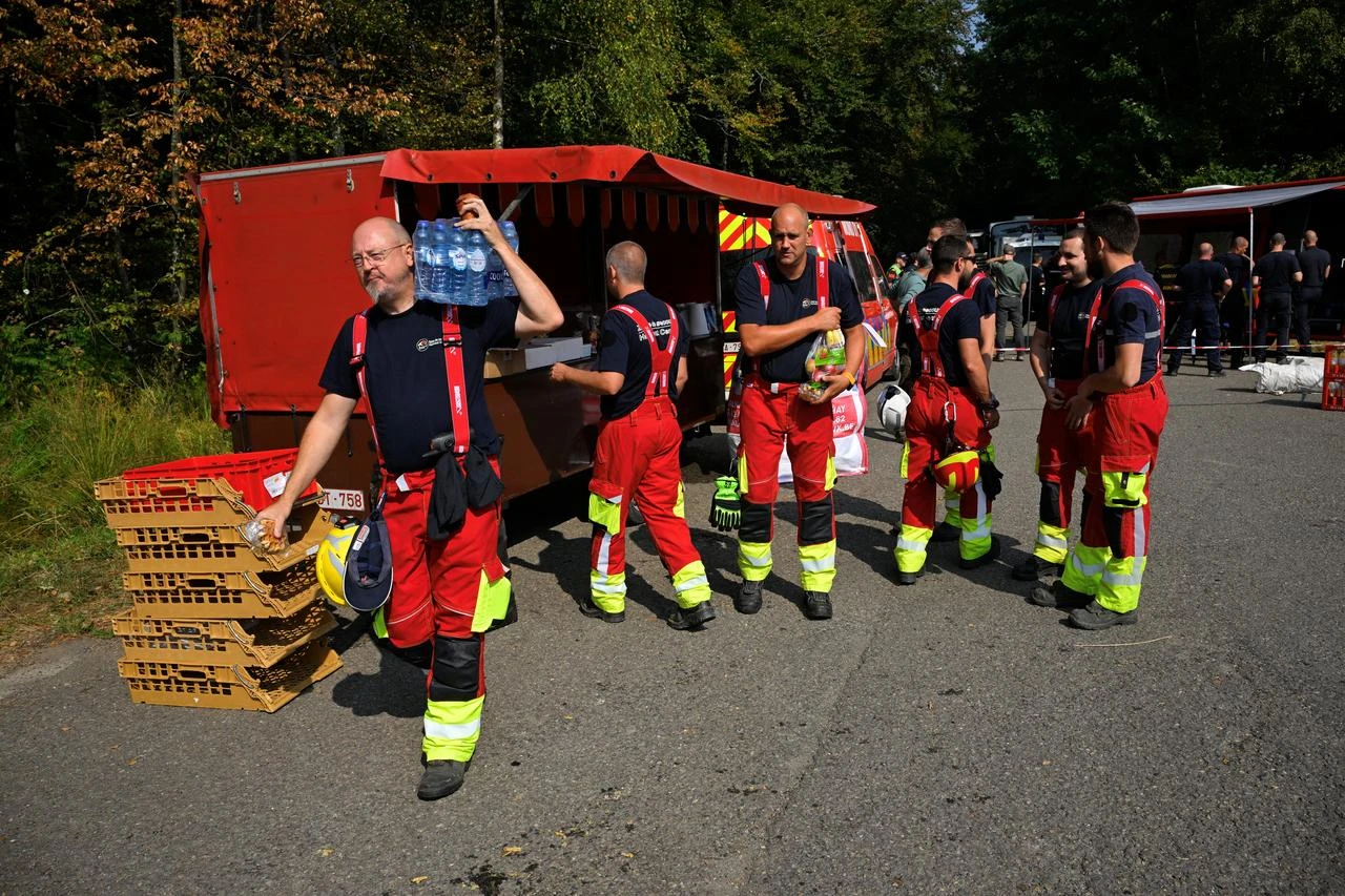 Firefighters gather at a Fire Service Logistics Support vehicle serving as a canteen to collect food and bottled water in Baelen, near Eupen, eastern Belgium, on August 14, 2026. (AFP Photo)