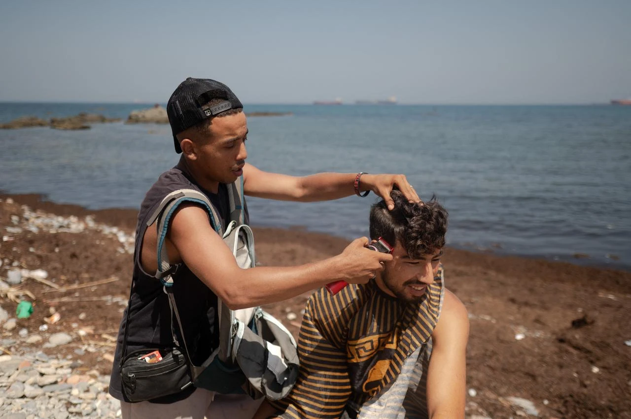 A migrant gets his hair done while waiting to enter a short-stay migrants centre, CETI, at Trampolin beach in Spain's north African Ceuta enclave on August 15, 2026. (AFP Photo)