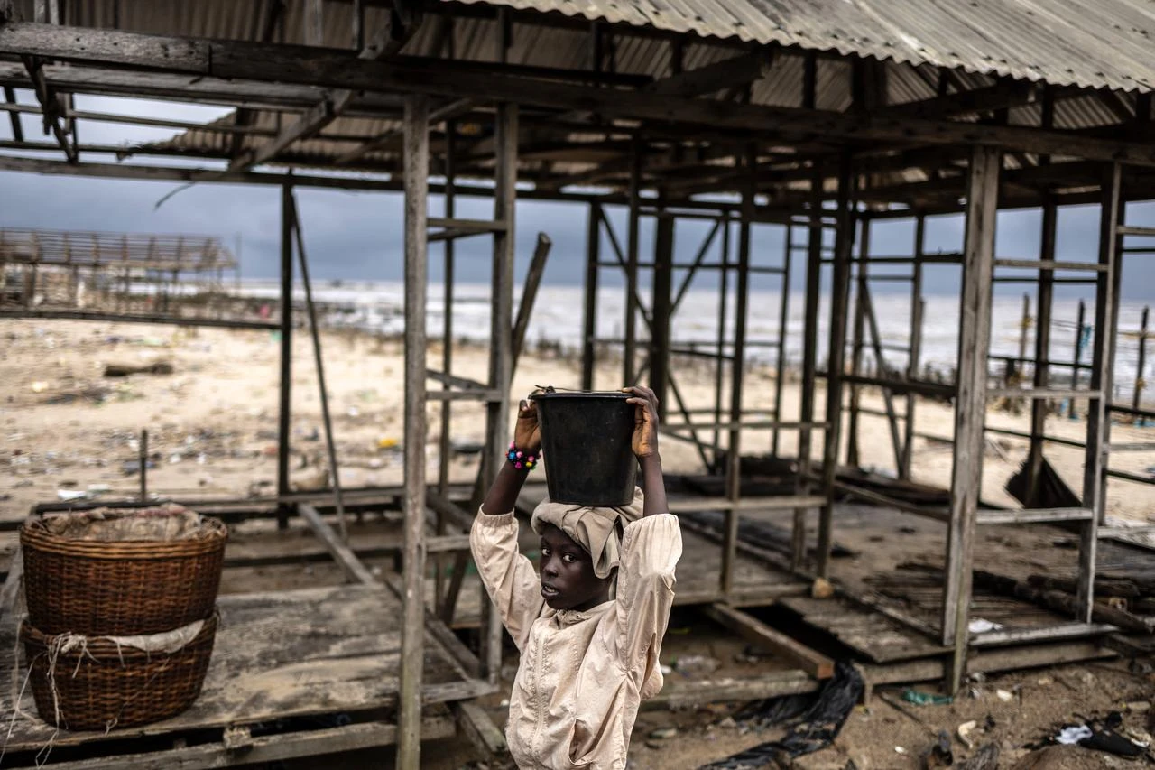 A resident looks on as she carries a bucket on her head past the remains of a building damaged by coastal erosion in Ayetoro, Ondo State, on August 6, 2026. (AFP Photo)