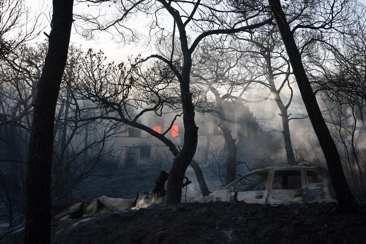 Smoke and flames rise among burned trees and damaged property during a wildfire in Peristeria on Salamina Island, near Athens, Greece, Aug. 16, 2026. (AA Photo)