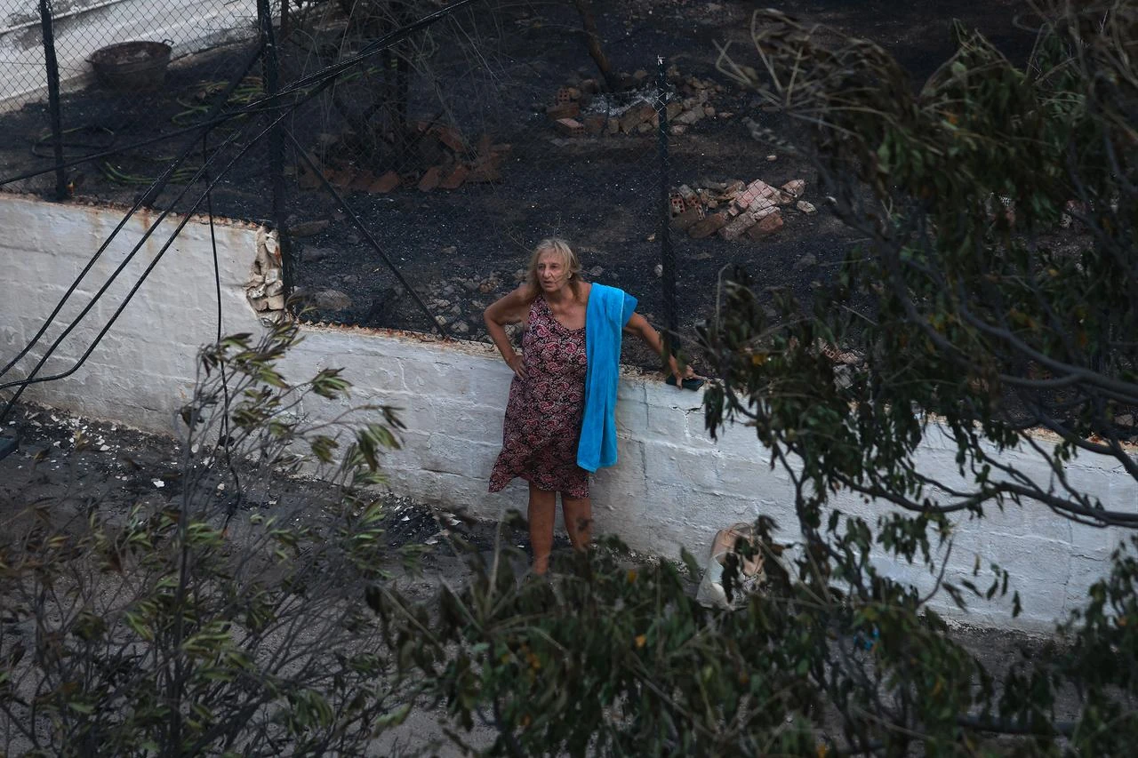 A resident stands amid burned vegetation and debris following a wildfire in Peristeria on Salamina Island, near Athens, Greece, Aug. 16, 2026. (AA Photo)