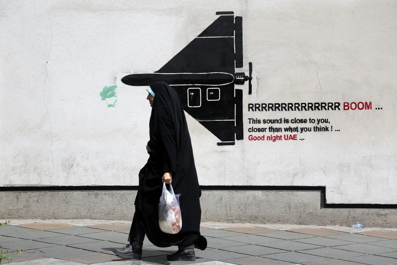 A woman walks past war-themed graffiti and murals painted on walls along the capital Tehran's streets and avenues as air defense systems are activated during the night while daily life continues in the shadow of rising military tensions between the US and Iran on July 22, 2026 in Tehran, Iran. (AA Photo)