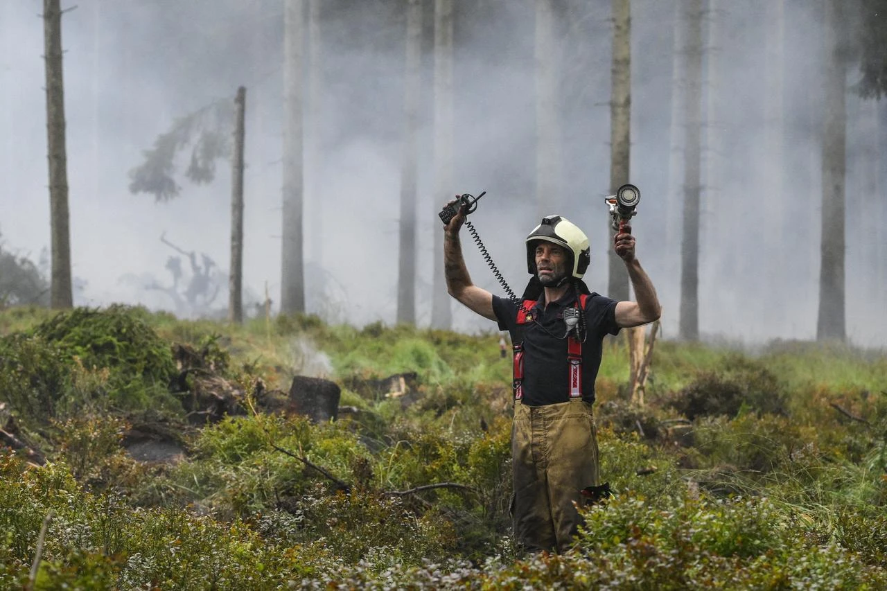 A firefighter gestures as smoke emanates from burnt vegetation during operations against a wildfire at the Hautes Fagnes (High Fens) nature reserve near Baelen, on August 18, 2026. (AFP Photo)