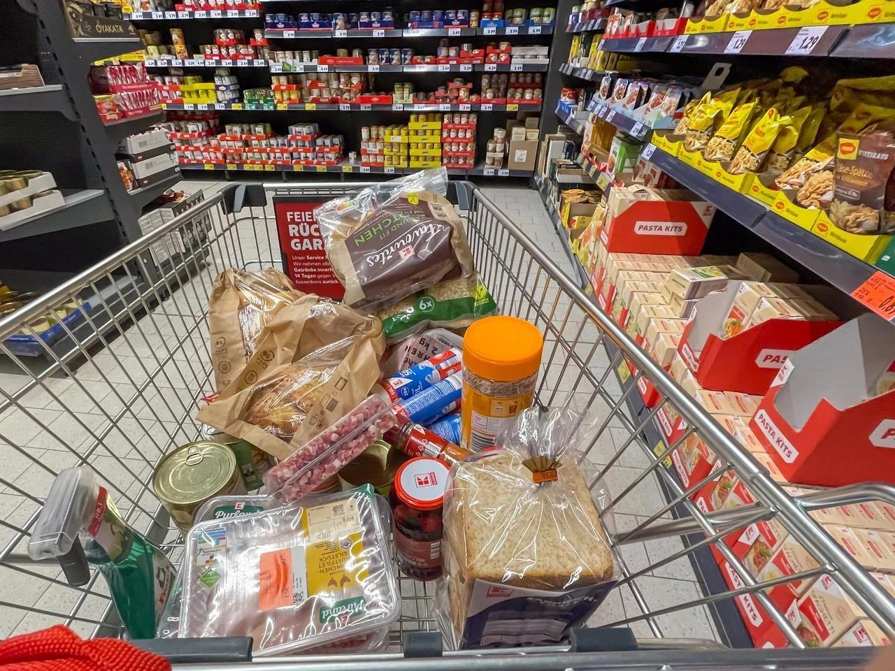 A shopping cart filled with groceries including bread, canned goods, and packaged food items in a supermarket aisle in Berlin, Germany, on February 19, 2025. (Adobe Stock Photo)