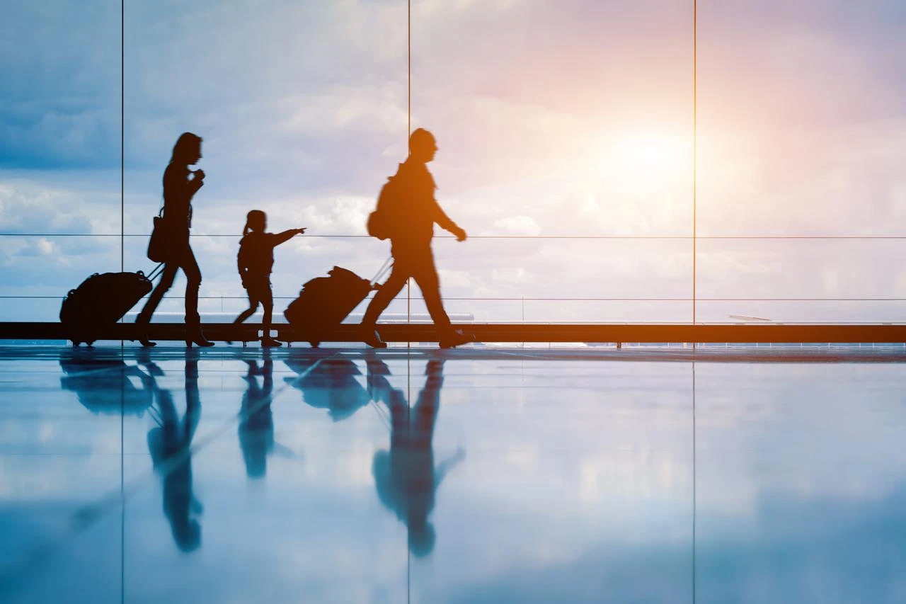 Family at airport travelling with young child and luggage walking to departure gate. (Photo via Adobe Stock)