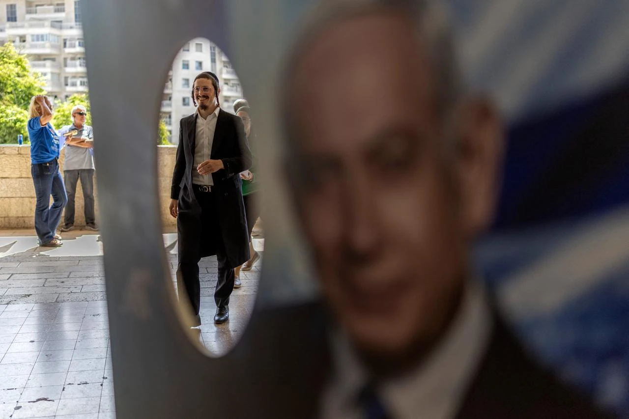 A member of Likud party is pictured through a poster with an image of Israeli Prime Minister Benjamin Netanyahu, at a polling station during primary elections of the party ahead of country's national elections, in Jerusalem on August 17, 2026. (AFP Photo)