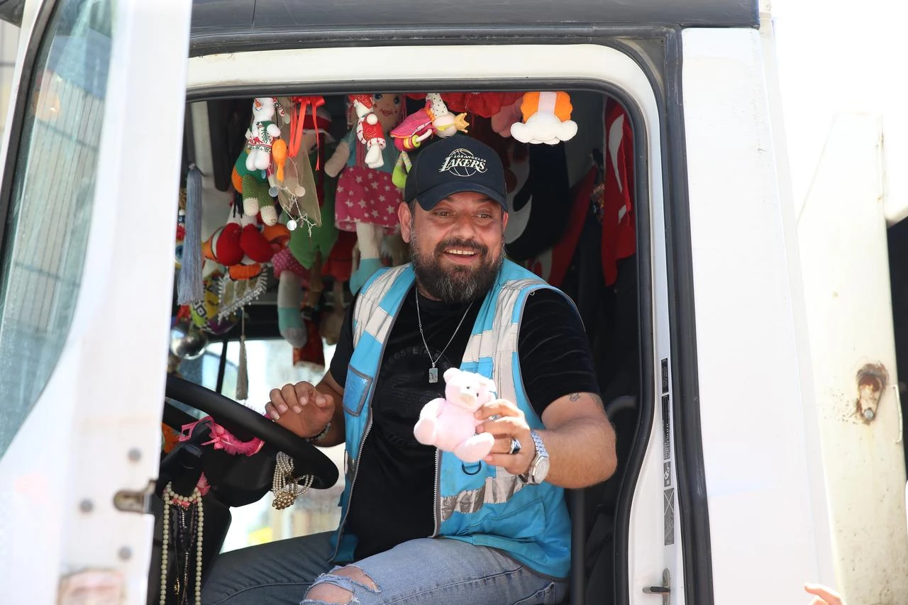 An Arsuz Municipality sanitation worker holds out a stuffed toy from the cab of his decorated garbage truck in Arsuz, Hatay, Türkiye, Aug. 23, 2026. (AA Photo)