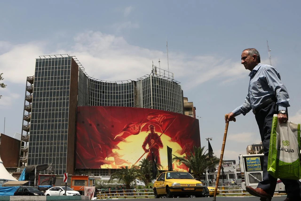People walk in front of a giant banner as daily life continues amid ongoing tensions between the United States in Tehran, Iran, on August 6, 2026. (AA Photo)