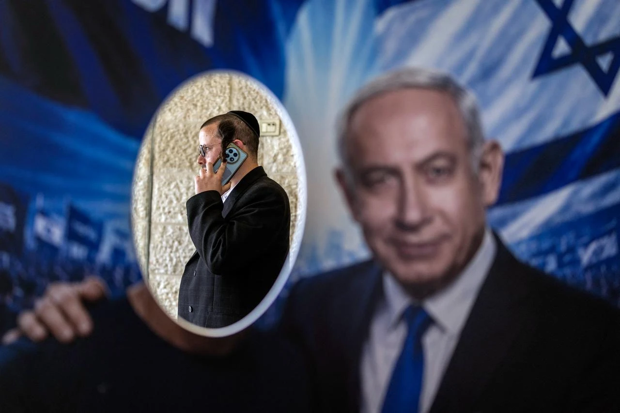 A member of Likud party is pictured through a poster with an image of Israeli Prime Minister Benjamin Netanyahu, at a polling station during primary elections of the party ahead of country's national elections, in Jerusalem on August 17, 2026. (AFP Photo)