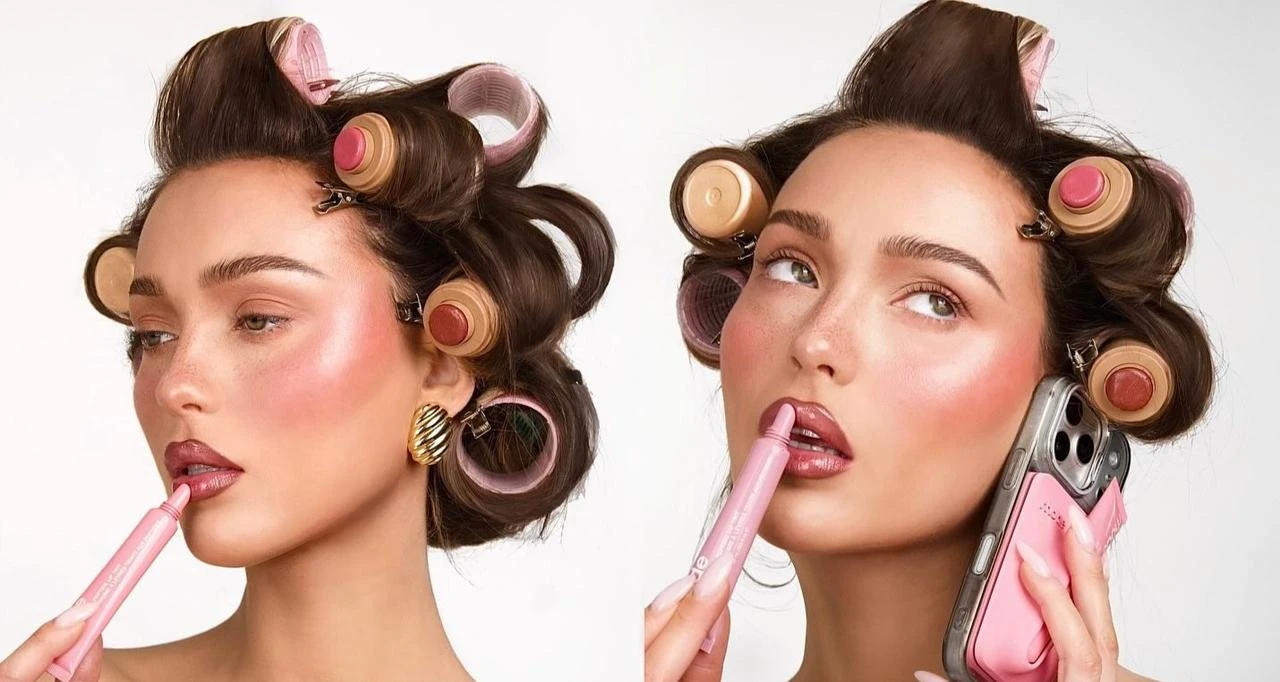 A woman poses with hair rollers while applying lip color and holding a smartphone. (Photo via X/@nermoeg)
